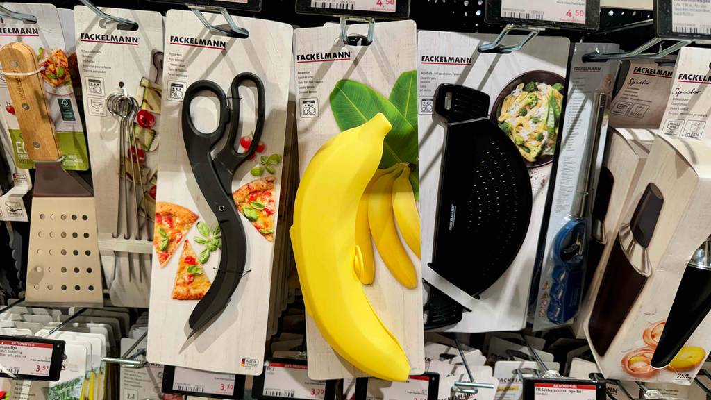 An einem Verkaufsregal hängt eine gelbe Bananenbox im Test neben anderen Haushaltsgegenständen.