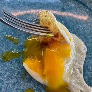 Eine Gabel sticht in ein Spiegelei auf einem blauen Teller