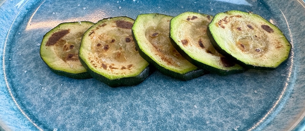 Fünf Scheiben angebratene Zucchinischeiben auf einem blauen Teller