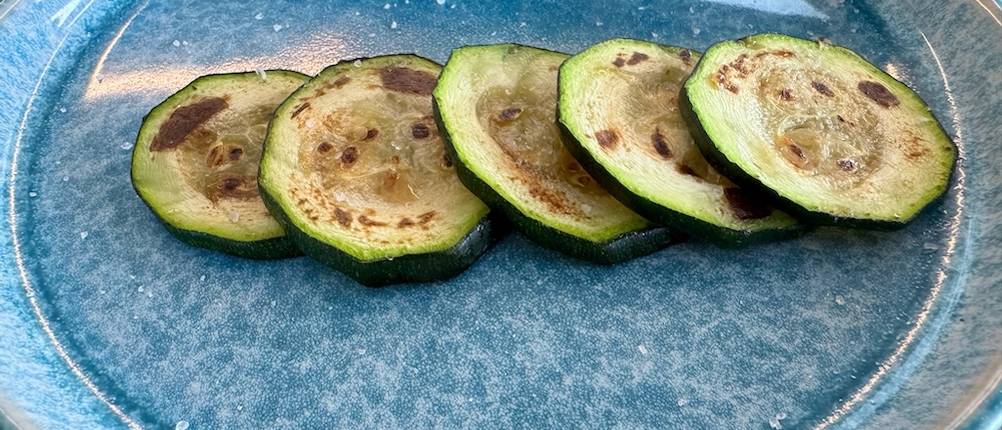 Fünf Scheiben angebratene Zucchinischeiben auf einem blauen Teller