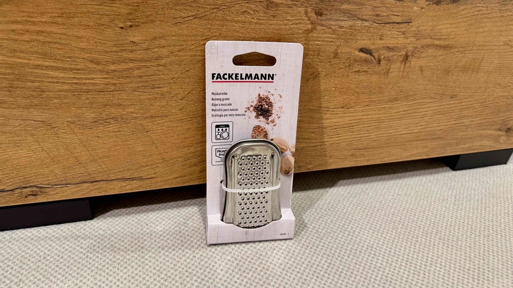 Eine Muskatreibe im Test steht in der Verpackung vor einer Holztruhe.