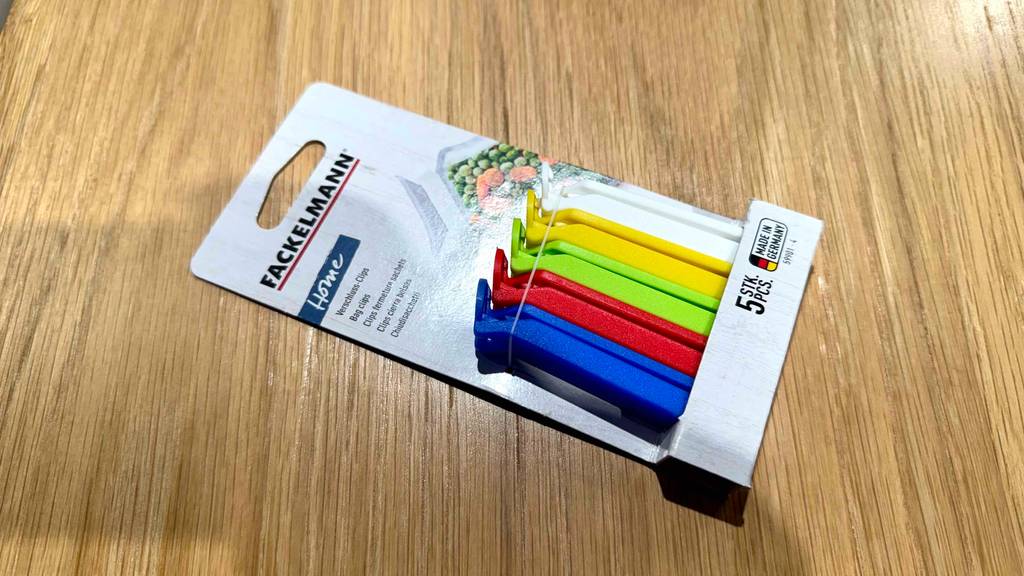 Fünf mehrfarbige Verschlussclips im Test liegen in ihrer Verpackung auf einem Holzbelag.