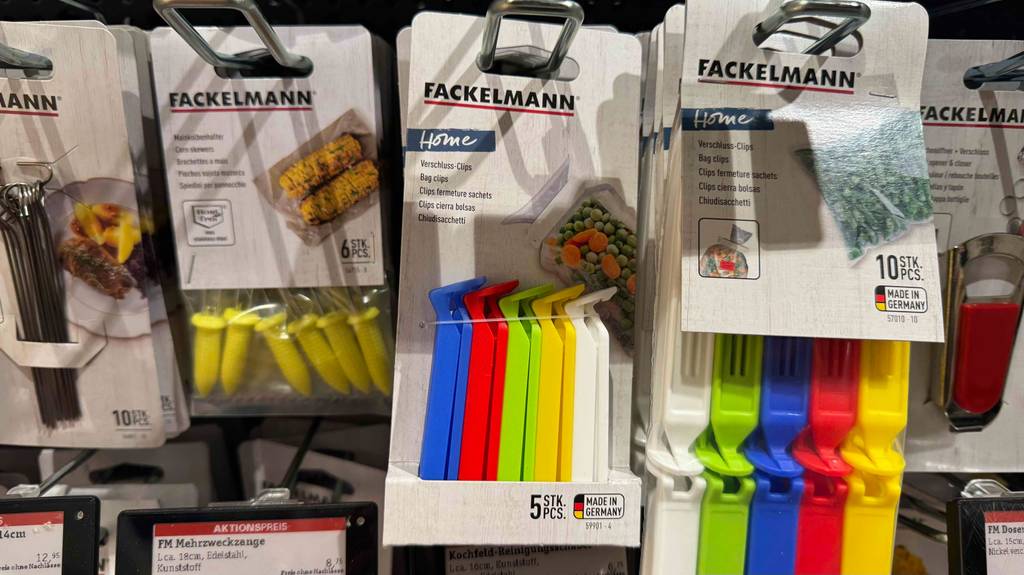 Mehrere Verpackungen mit getesteten Verschlussclips in unterschiedlichen Farben hängen an einem Verkaufsregal neben weiteren Haushaltsutensilien von Fackelmann.
