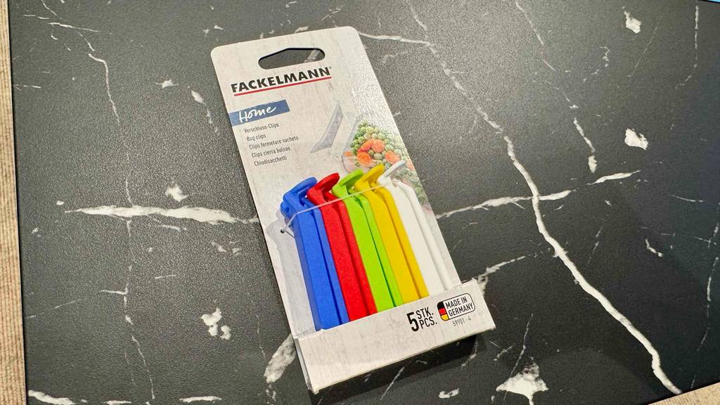 Fünf farbige Verschlussclips im Test in der Verpackung liegen auf einer marmorierten Unterlage.