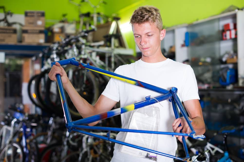 Ein junger Mann hält den Rahmen eines Fahrrads in einem Fahrrad-Laden.