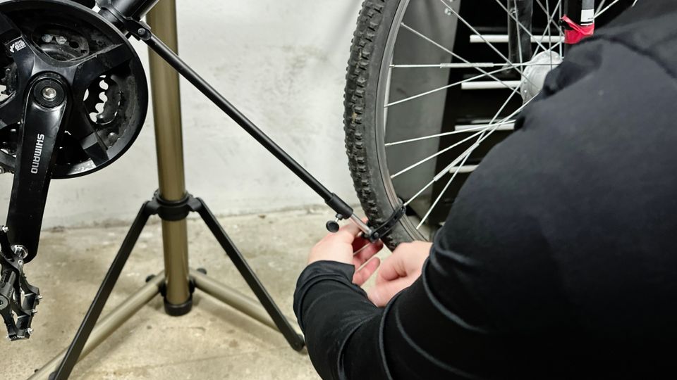 Eine Person befestigt eine Stütze am Cxwxc Fahrrad-Montageständer, um das Vorderrad zu stabilisieren.