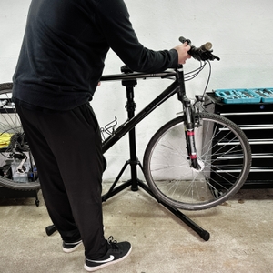 Eine Person setzt ein Fahrrad in den Montageständer ein. Der Rahmen wird in der Klemmung fixiert.