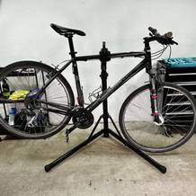 Ein Fahrrad ist sicher in einem Montageständer eingespannt. Im Hintergrund befinden sich Werkstattregale mit Werkzeugen.