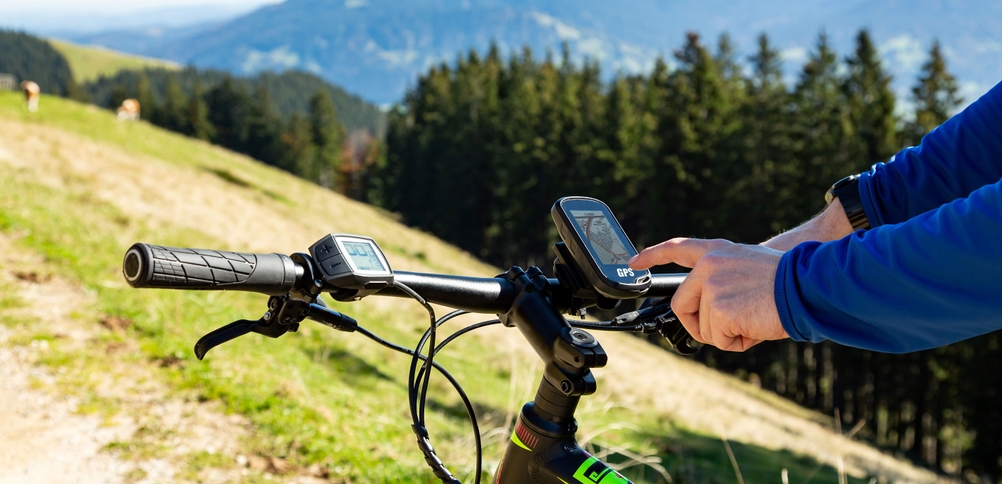 Bedienung eines Fahrrad-Navis mit Berglandschaft im Hintergrund.