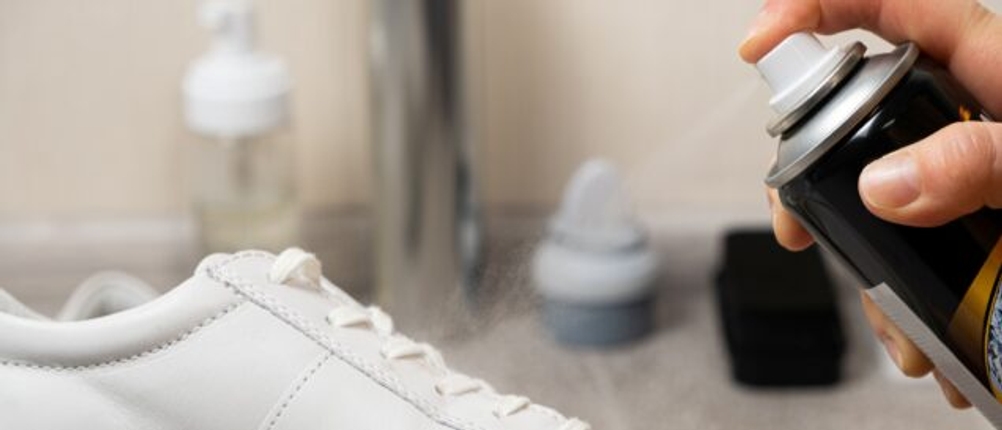 Ein weißer Sneaker wird mit Imprägnierspray behandelt.