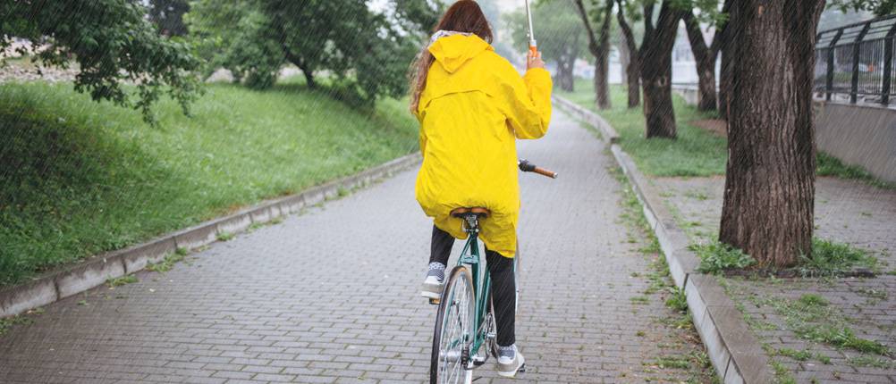 Rückansicht einer Frau mit Regenkleidung und Schirm auf dem Fahrrad
