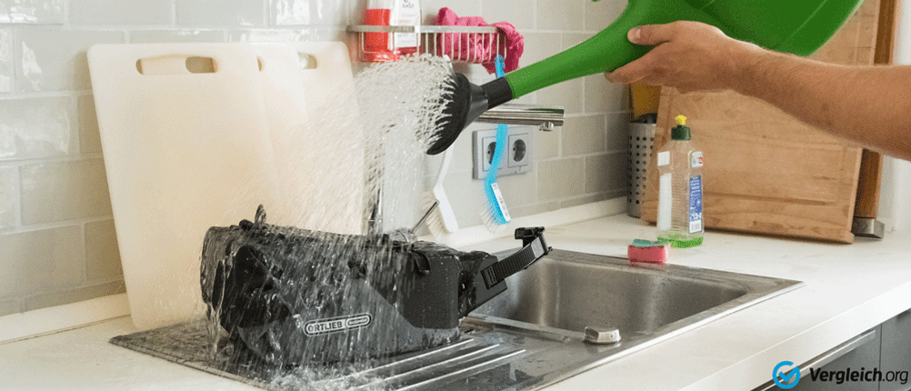 Eine Person schüttet mit einer Gieskanne Wasser auf eine Fahrrad-Satteltasche.