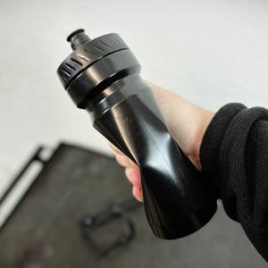 Eine Hand drückt die BBB Cycling Wasserflasche zusammen, um die Flexibilität des Materials zu testen. Im Hintergrund ist eine zweite Flasche leicht unscharf zu sehen.