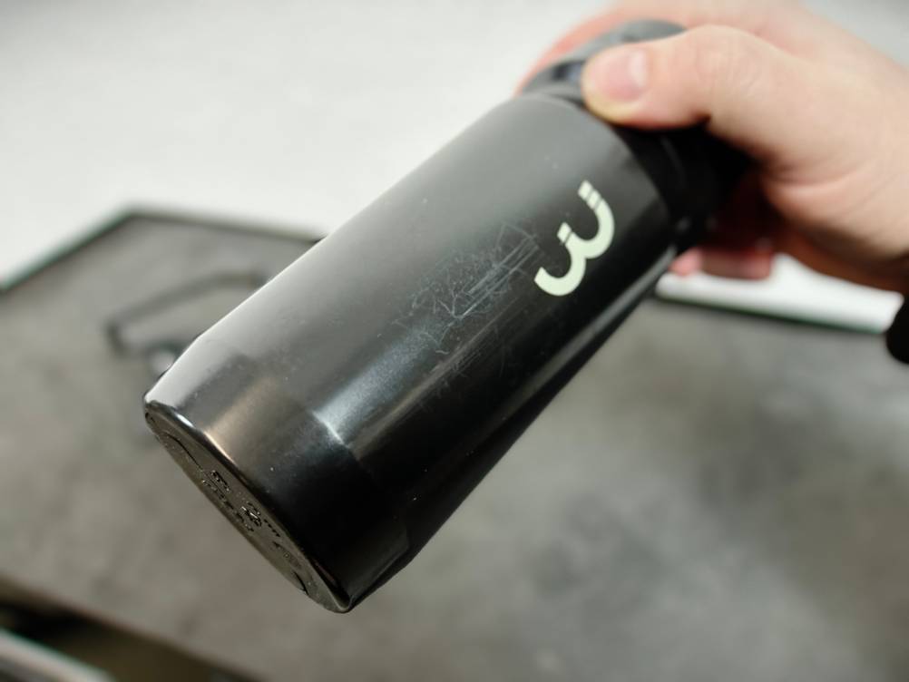 Eine schwarze BBB Cycling Wasserflasche wird in einer Hand gehalten und zeigt deutliche Kratzer auf der Oberfläche. Besonders am unteren Bereich sind Gebrauchsspuren sichtbar.