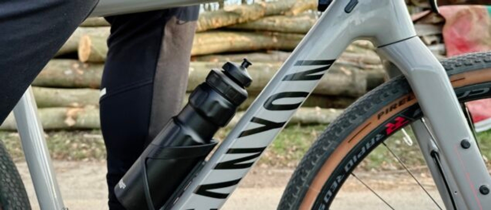Ein Radfahrer mit schwarzer Sportkleidung fährt ein Canyon Gravelbike, während die SIGG WMB Sports Trinkflasche am Rahmen befestigt ist.