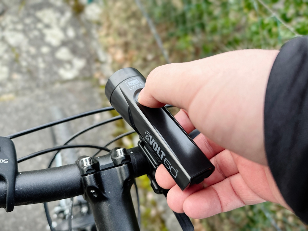 Das Cateye GVolt 60 wird von einer Hand am Lenker eines Fahrrads befestigt. Die kompakte Bauweise der Lampe ist deutlich erkennbar.