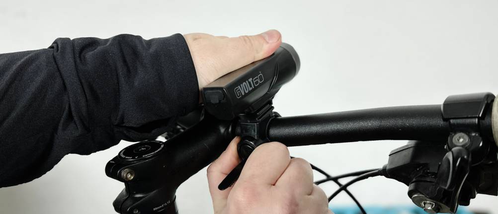 Eine Person befestigt das Cateye GVolt 60 am Lenker eines Fahrrads. Die Halterung wird mit einer Hand festgezogen.