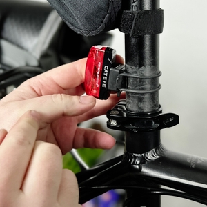 Eine Person befestigt das Cateye GVolt 60 Rücklicht an der Sattelstütze eines Fahrrads. Die Halterung wird mit einer Hand fixiert.