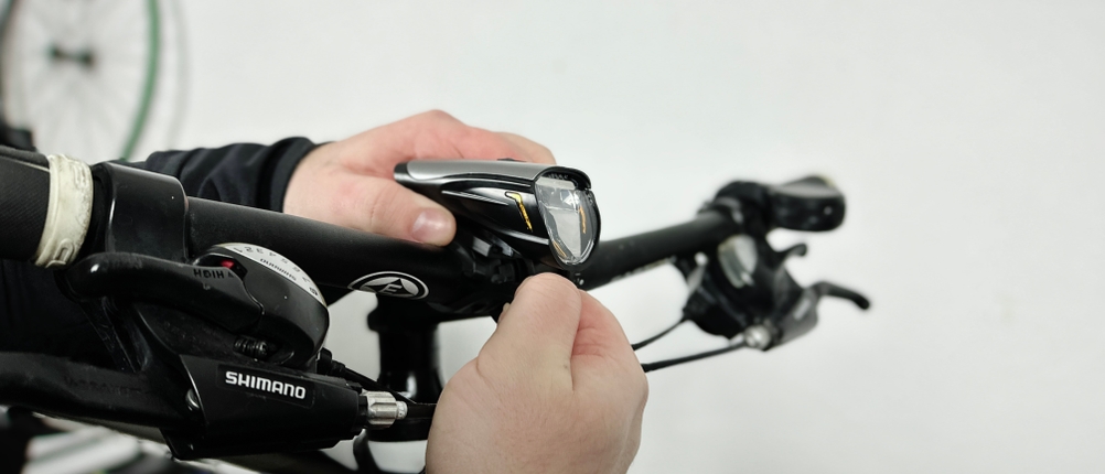 Eine Person befestigt das Deilin BL12 Frontlicht am Lenker eines Fahrrads. Die Halterung wird mit einer Hand fixiert.