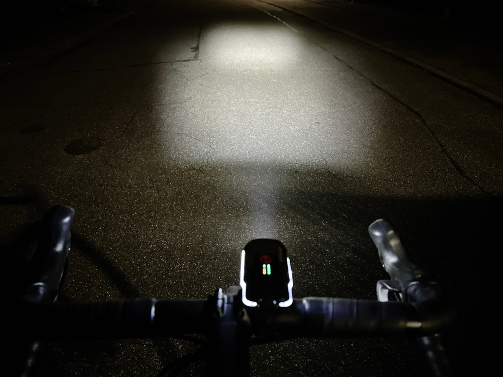 Die Frontleuchte des Sigma Sport Aura 80 Blaze wirft einen breiten Lichtkegel auf die dunkle Straße. Die gleichmäßige Ausleuchtung sorgt für klare Sicht im Dunkeln.