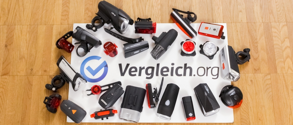 Fahrradbeleuchtung-Test: unterschiedliche Fahrradbeleuchtungsmodelle auf einem Vergleich.org-Schild, das auf einem hellen Holzboden liegt