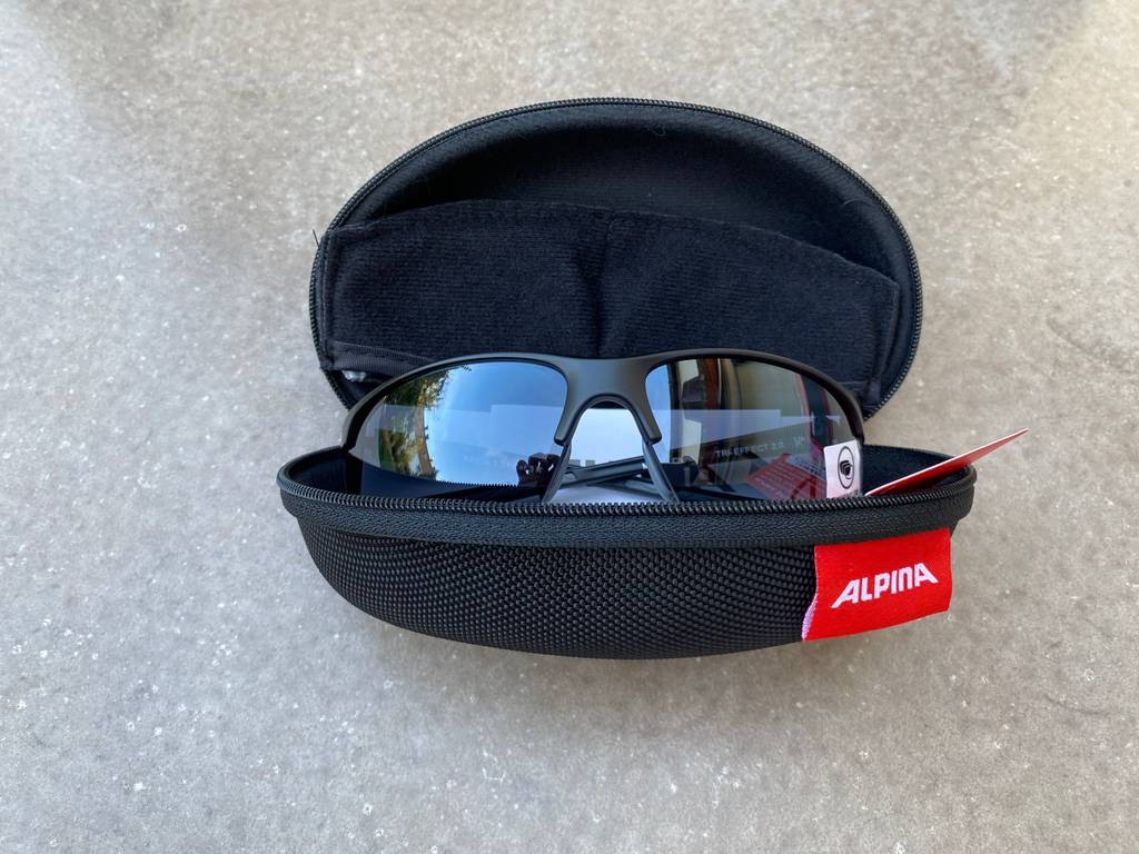 Fahrradbrillen-Test: Fahrradbrille Alpina liegt in ihrem Etui auf grauem Untergrund. 
