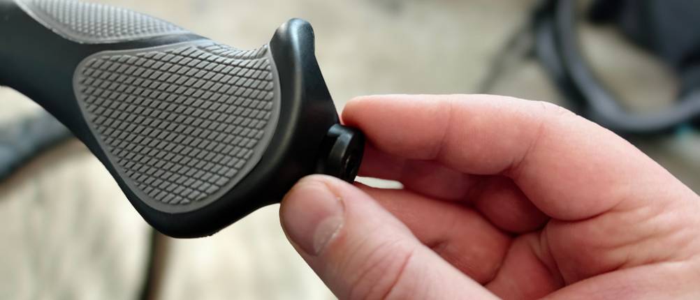 Eine Hand hält eine Endkappe an das Griffende eines montierten Fahrradgriffs. Die Endkappe wird gerade angesetzt.