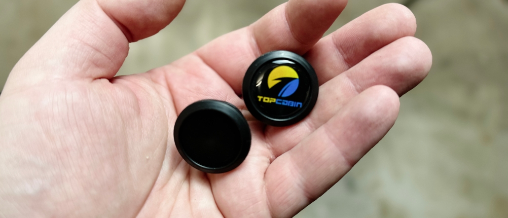 Zubehör der Topcabin-Fahrradgriffe in Nahaufnahme. Zu sehen sind zwei Endkappen, eine mit Logo, eine ohne.