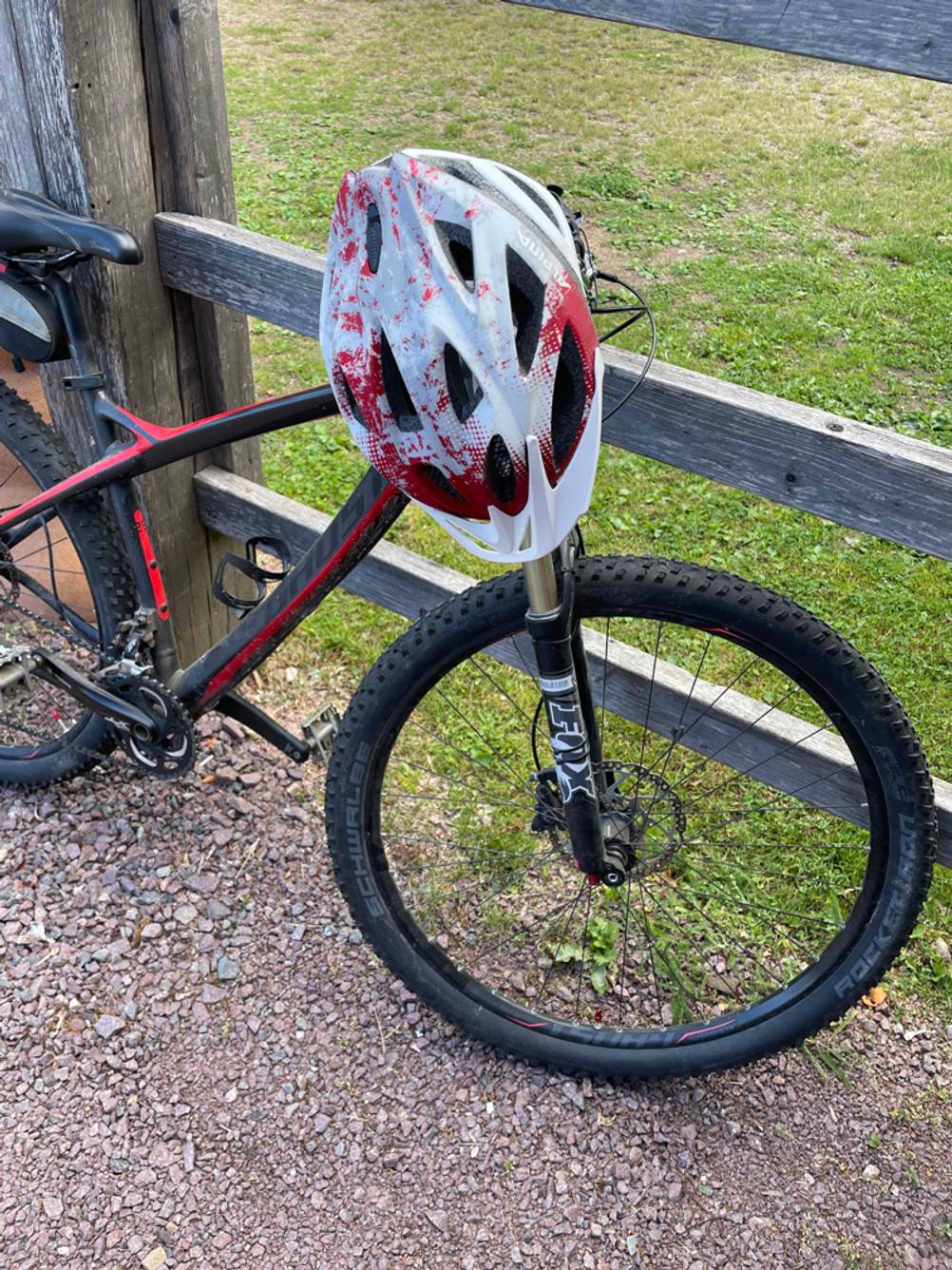 Fahrradhelm-Test: Fahrradhelm, der über dem Lenkergriff eines Mounbikes, das einem Holzzaun lehnt, hängt