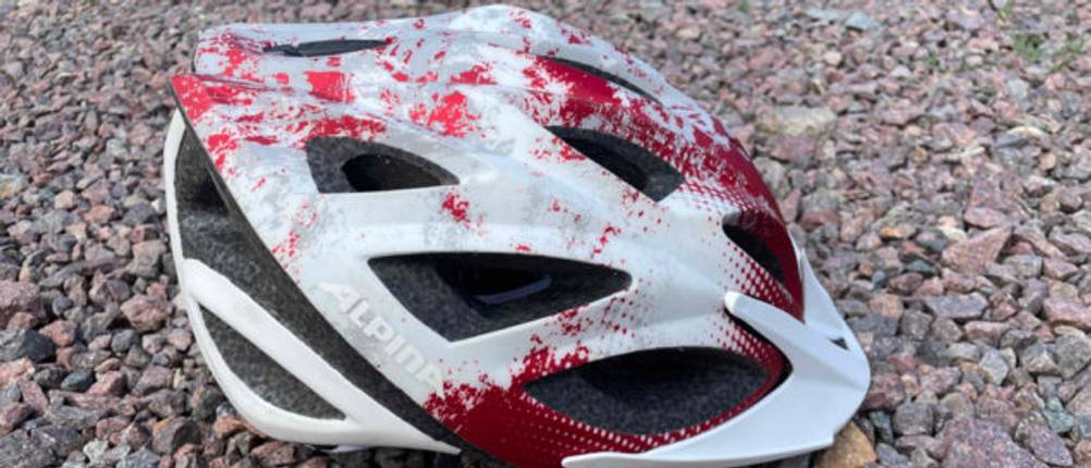 Fahrradhelm-Test: Nahaufnahme eines Fahrradhelm in rot-weißem Design auf steinigem Untergrund