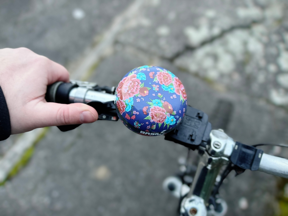 Die Basil-Big-Bell-Bloom-Fahrradklingel ist am Lenker eines Fahrrads montiert. Eine Hand betätigt den Hebel, um die Klingel auszulösen.