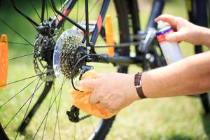 Ein Mann mit einem Lappen in der linken und einer Sprühdose in der rechten Hand reinigt ein Fahrrad.