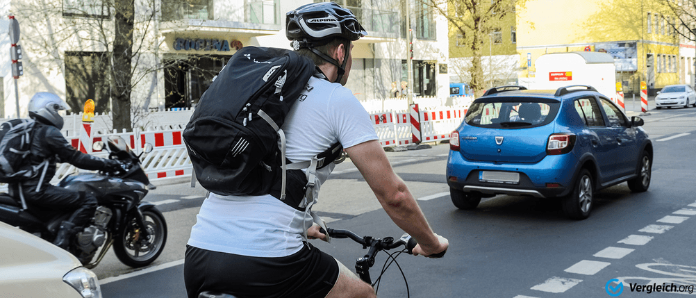 Ein Mann fährt mit Fahrradrucksack und Helm auf seinem Fahrrad durch eine Stadt.