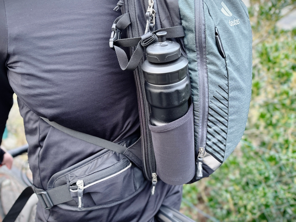 Am Deuter Compact EXP 14 ist eine schwarze Trinkflasche seitlich im Netzfach verstaut. Das Fach liegt gut erreichbar außen am Rucksack.
