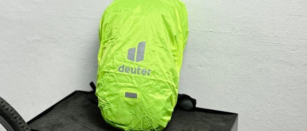 Der Deuter Compact EXP 14 ist mit einer leuchtend grünen Regenhülle abgedeckt. Das Deuter-Logo ist gut sichtbar aufgedruckt.
