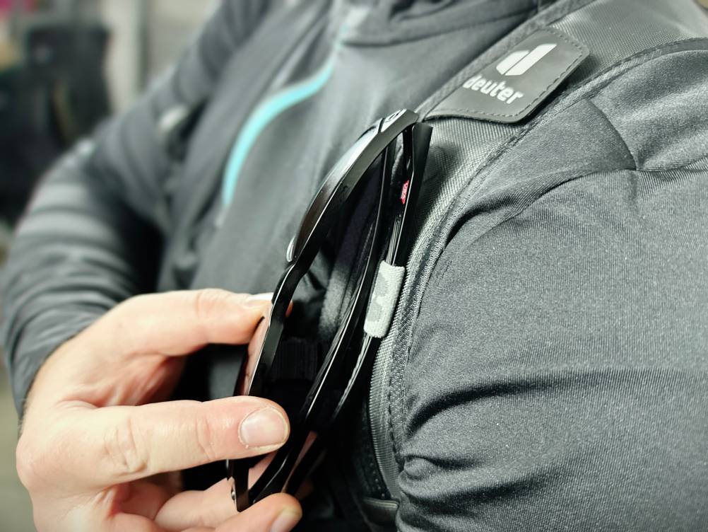 Eine Sonnenbrille wird an einer kleinen Halteschlaufe am Schultergurt des Deuter Compact EXP 14 befestigt. Die Befestigung erfolgt über ein flexibles Band.