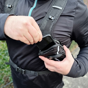 Ein Smartphone wird in die Brusttasche des Toptrek-Fahrradrucksacks gesteckt. Die Tasche befindet sich direkt am Schultergurt.
