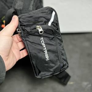 Die abnehmbare Zusatztasche des Toptrek-Fahrradrucksacks wird in der Hand gehalten. Sie ist mit Reißverschluss und Logo versehen.