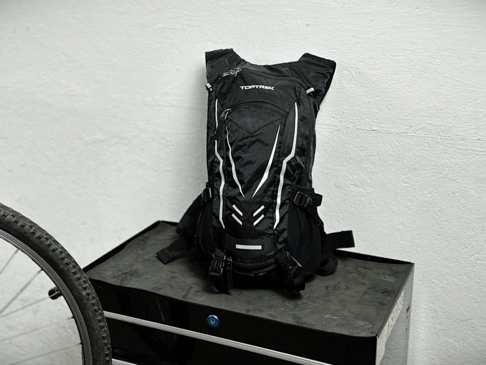 Der Toptrek-Fahrradrucksack steht aufrecht vor einer weißen Wand. Die Frontseite zeigt mehrere Fächer und reflektierende Elemente.