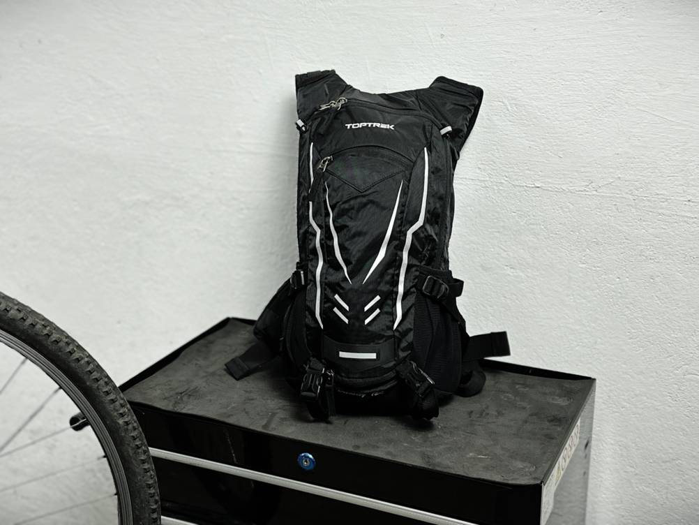 Der Toptrek-Fahrradrucksack steht aufrecht vor einer weißen Wand. Die Frontseite zeigt mehrere Fächer und reflektierende Elemente.