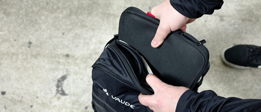 Ein Laptop wird in das Hauptfach des Vaude Tremalzo 22 gelegt. Der Rucksack liegt dabei offen auf dem Boden.