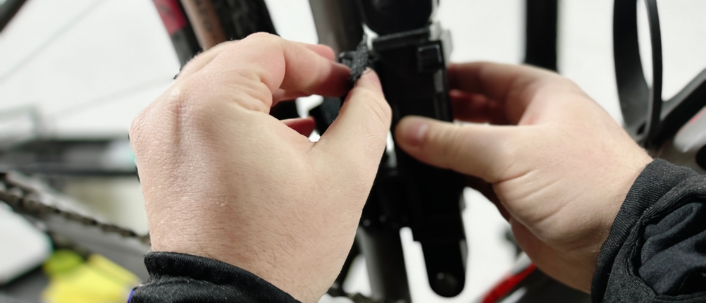 Eine Person montiert die Halterung des Fischer-Faltschlosses am Fahrradrahmen. Die Befestigung erfolgt mit einem Klettband.