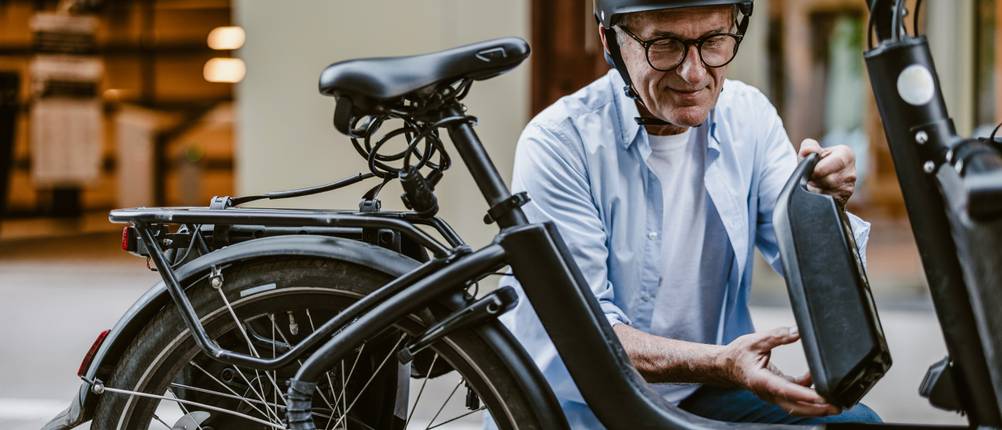 Fahrradversicherungen im Test: Ein älterer Herr bringt den Akku an seinem E-Bike an.