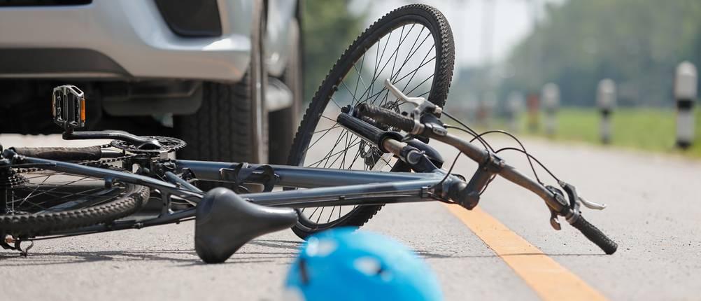 Während ein Auto im Hintergrund steh, liegen ein defektes Fahrrad und ein Helm auf der Straße.