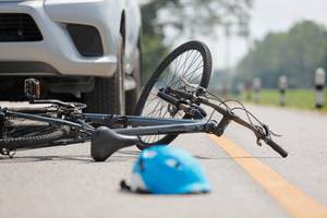 Fahrradversicherungen im Test: Während ein Auto im Hintergrund steh, liegen ein defektes Fahrrad und ein Helm auf der Straße.