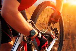 Fahrradversicherungen im Test: Eine Person mit Fahrradhandschuhen repariert die Kette eines Fahrrads.