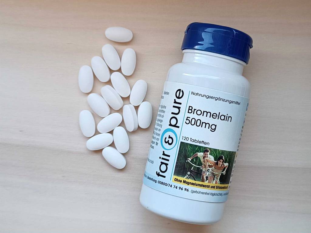 Eine Kunststoffdose inklusive Tabletten mit getestetem Bromelain Wert liegt neben weißen Tabletten.