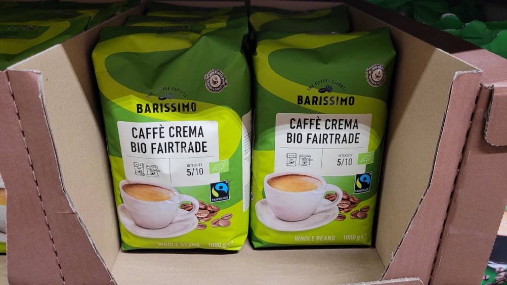 Mehrere Packungen der Fairtrade-Kaffeebohnen im Test in einem Karton in einem Regal.