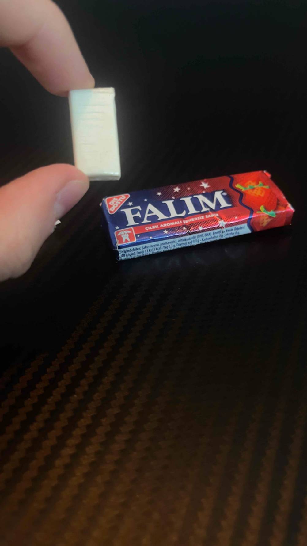 Eine Hand hält einen ausgepackten Falim-Kaugummi im Test vor die Verpackung.