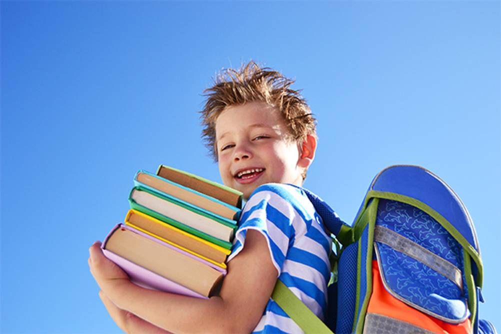Familando-Schulranzen im Test: Ein Junge mit Schulranzen und einem Stapel Bücher auf dem Arm.